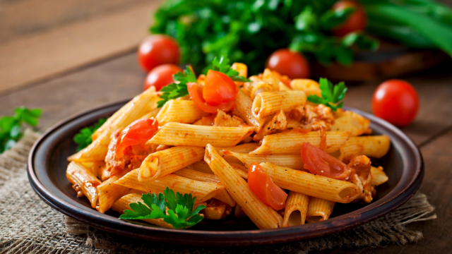 Penne pasta in tomato sauce with chicken and tomatoes  on a wooden table