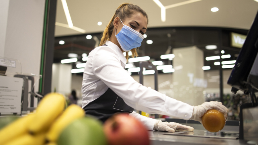 Female cashier in supermarket wearing hygienic protection mask and gloves while working risky job because of corona virus pandemic.