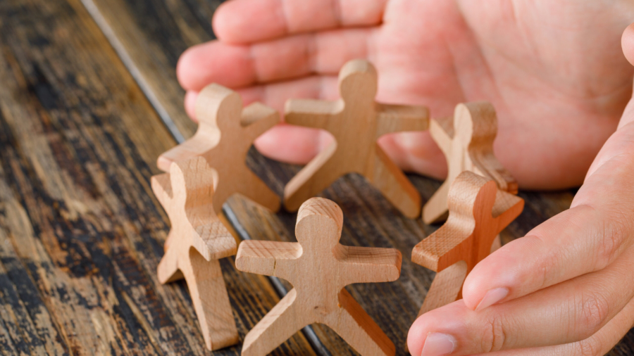 Business success concept on wooden background high angle view. hands protecting wooden figures of people.