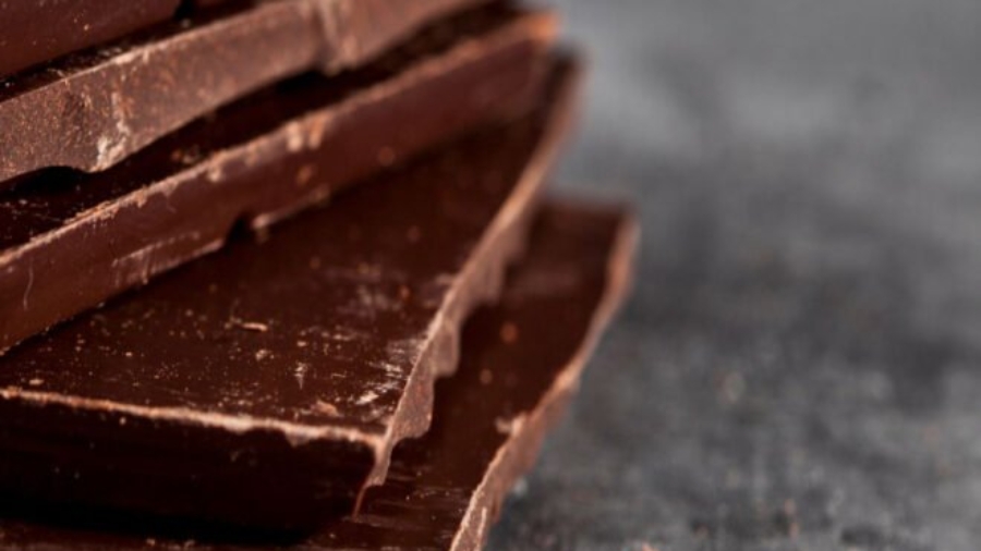 Dark chocolate bar pieces closeup. Sweet food photo concept. The chunks of broken chocolate stacked on grey background.