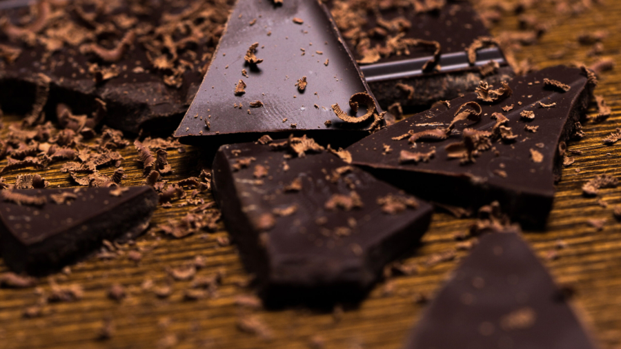 Dark chocolate bar and some powder around it on a wooden surface