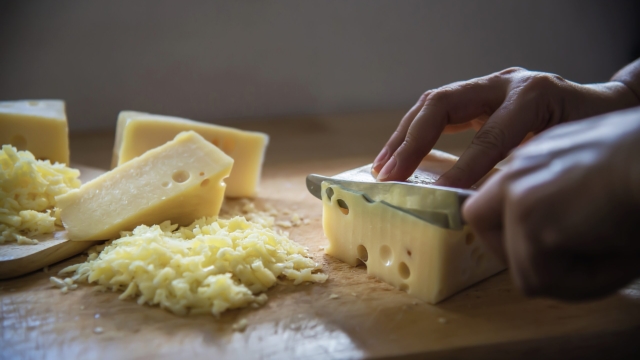 Woman cut slice cheese for cook using knife in the kitchen - people making food with cheese concept